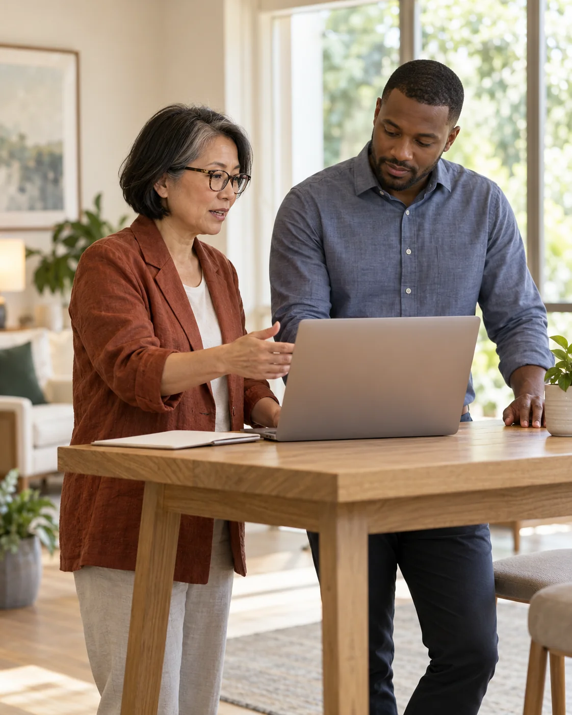 A female operations lead and a male admissions colleague review next steps at a standing-height work table with a laptop turned away
